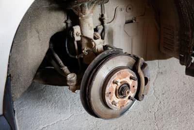 Worn brake rotor, pad, and caliper with wheel and tire removed
