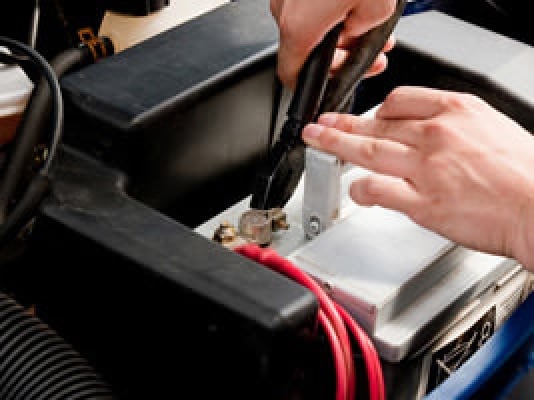 Hands using nut pliers on car battery connection