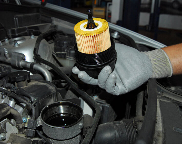 Technician's gloved hand holding fresh new oil filter above car's engine