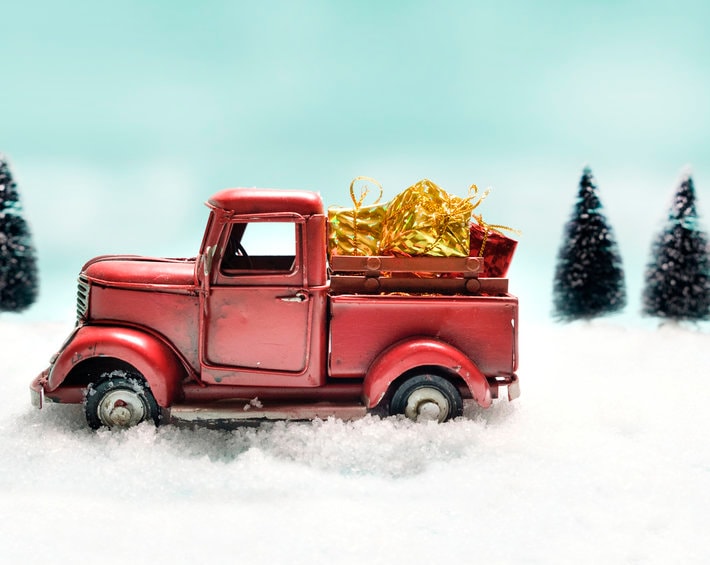 Red truck toy carrying a christmas gift on sweet pastel retro turquoise color background.