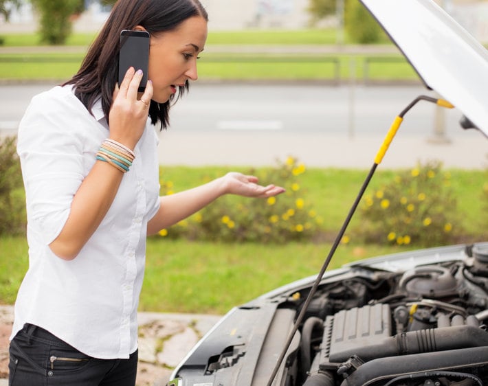 Woman standing next to broken car and talking on the phone