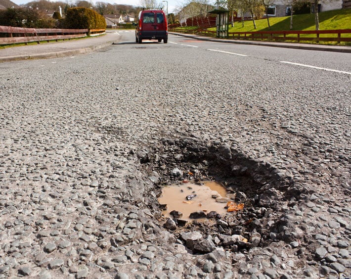 Car driving away from water-filled pothole in asphalt road