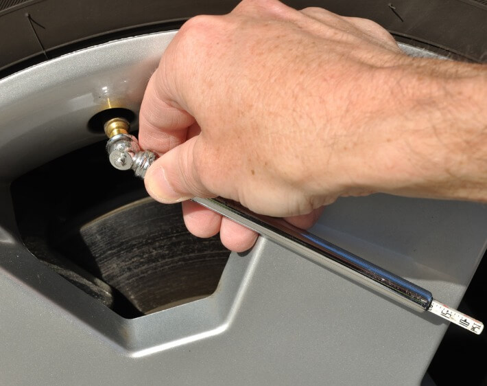 mans hand checking tire pressure with air pressure gauge