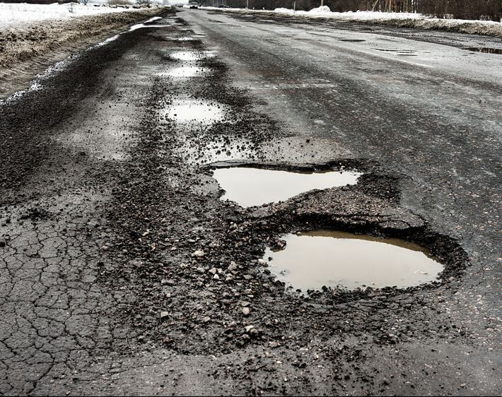 asphalt highway with several potholes full of melting snow