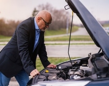 Man with glasses on the side of the rood looking under his car's hood