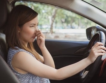 Woman holding her nose while driving 