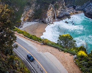 Aerial view of car cruising highway running along the coast