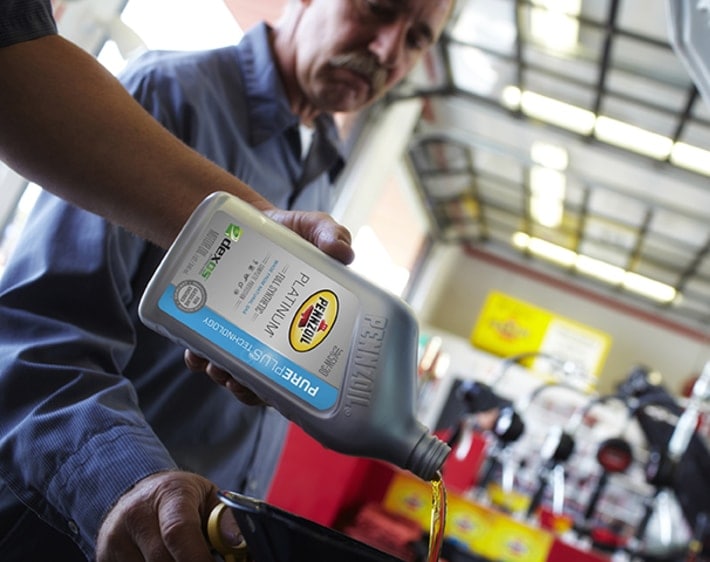 Firestone Complete Auto Care technician pouring Pennzoil Platinum oil into engine