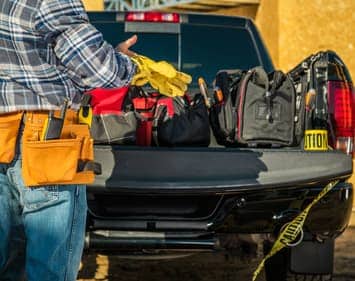Blue Collar Man Wearing Safety Gloves in Front of His Pickup Truck Full of Necessary Tools.