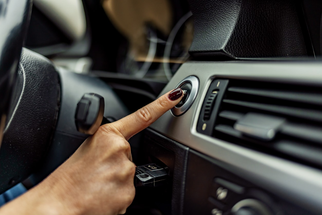 Woman with burgundy colored polish pressing push to start button in vehicle