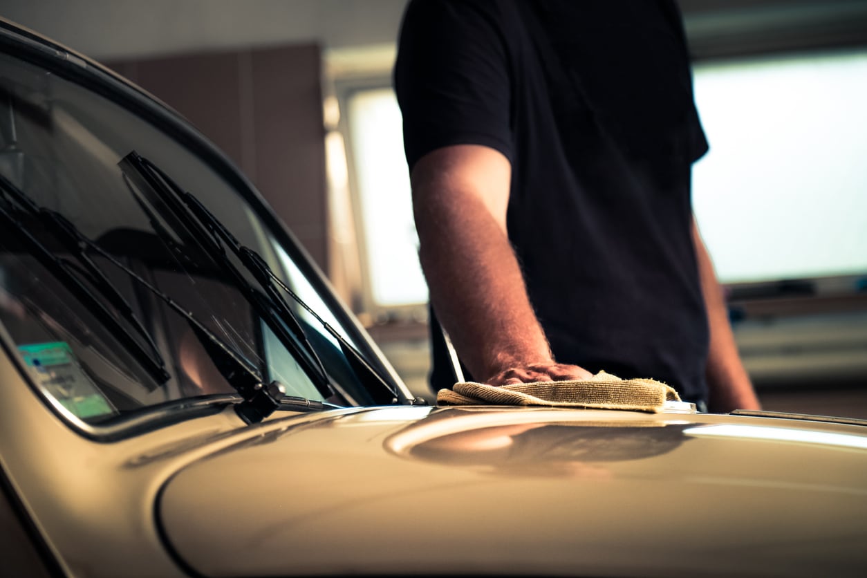Man in garage with cleaning rag in hand as he polishes a classic car in his garage