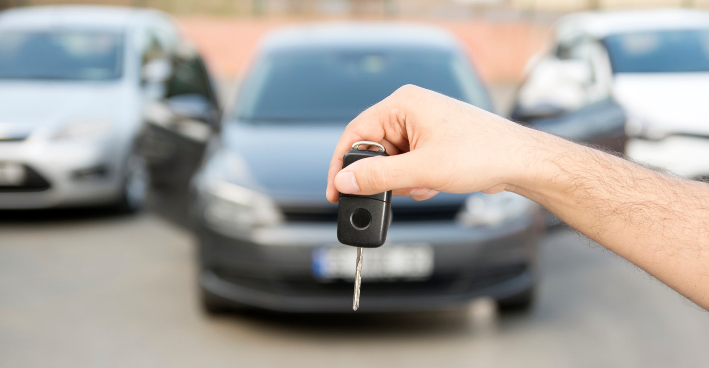 Image focus on person holding car key with blurred vehicle in background.