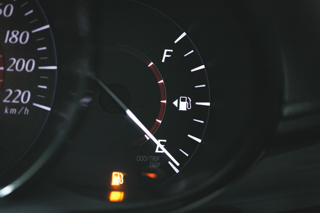 Vehicle dashboard with an illuminated gas light and a gas gauge close to "E," both indicating low fuel in the vehicle